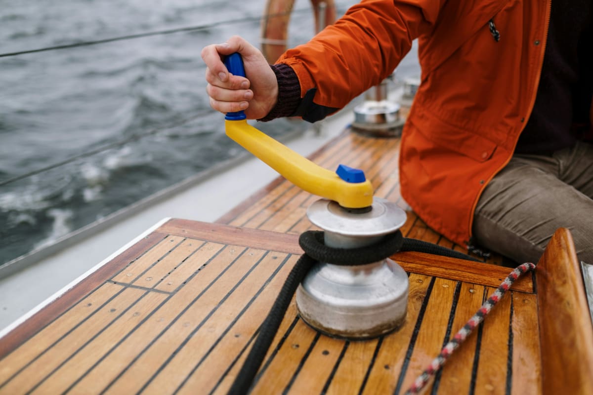 Person using a winch handle to trim a rope on a sailboat deck.