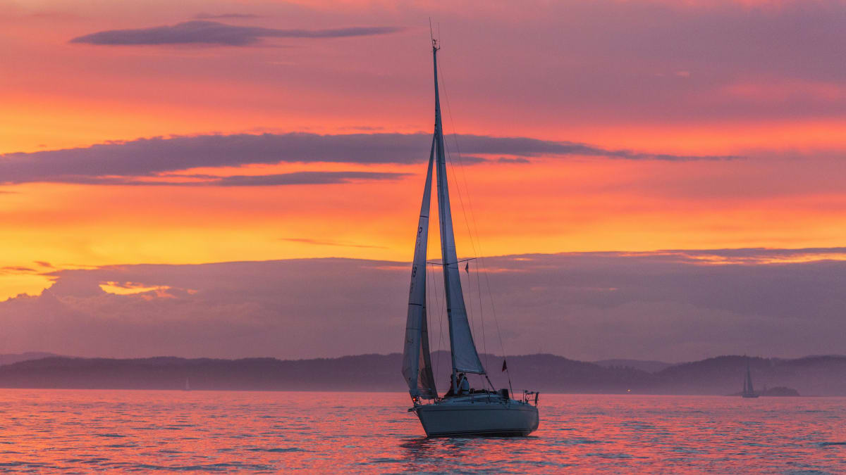 Sailboat sailing on calm water at sunset with a vibrant orange and pink sky in the background.