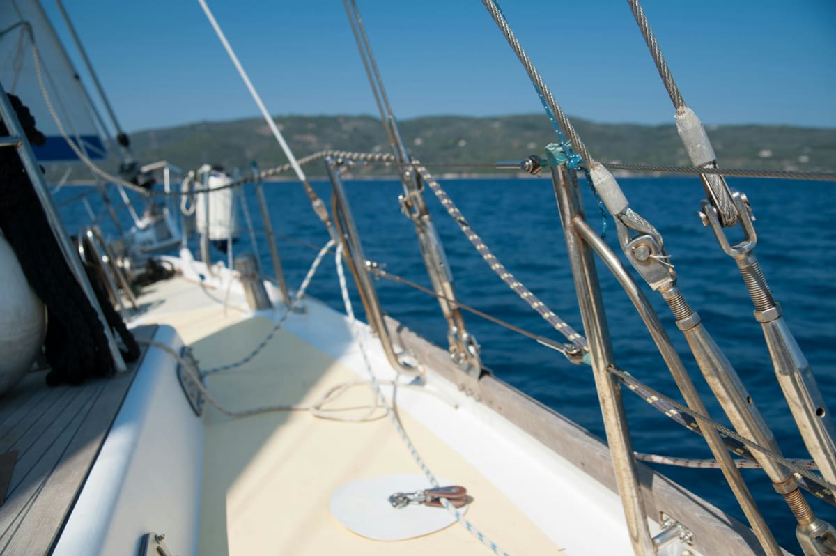 Close-up view of sailboat deck rigging and lifelines with blue ocean and hills in the background.