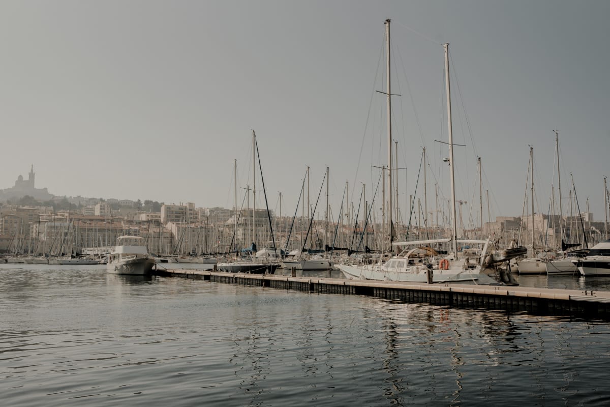 Marina with sailboats docked on calm water under a soft, hazy sky