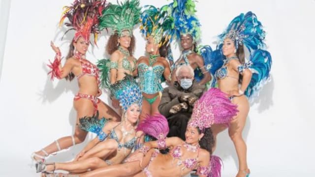 SambaViva dancers in full Carnaval costume with Bernie Sanders sitting in the middle wearing a coat and mittens