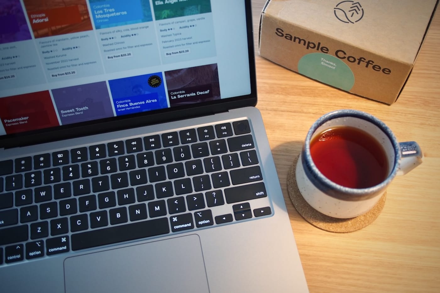 Laptop showing Sample Coffee website, sitting on a table next to a speckled ceramic mug with coffee