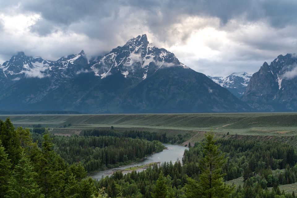 A river in front of mountain peaks with dark clouds looming in the sky.