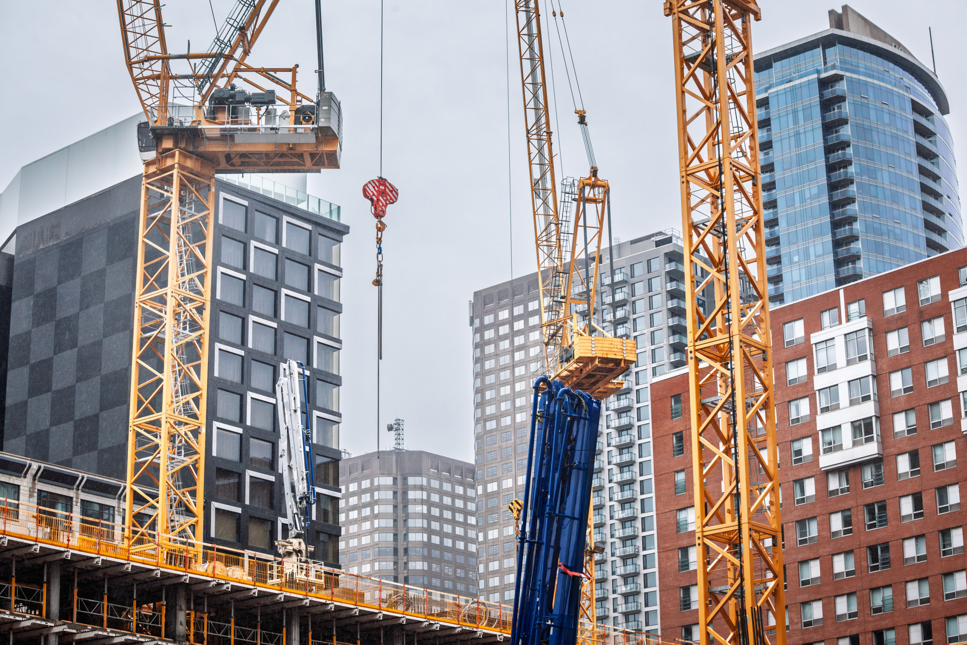 Tower cranes lift heavy sections on a new high rise build in downtown Montreal while existing condo towers frame the scene, capturing rapid skyline growth and the dense construction climate of Canada.