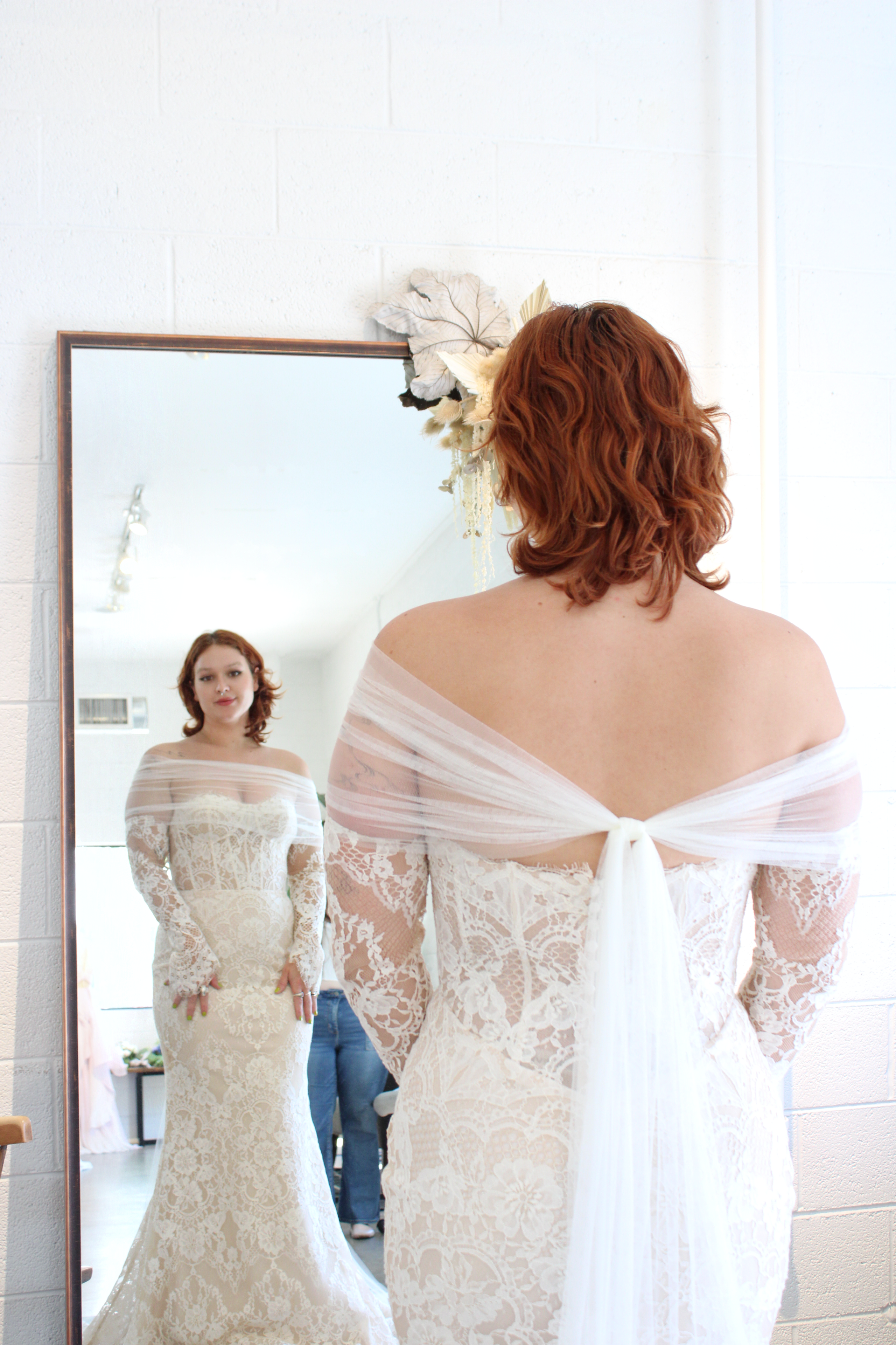 woman at a bridal salon looking into a mirror wearing a bridal scarf like a shrug