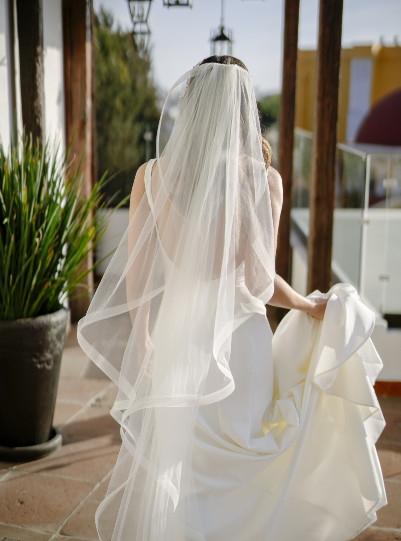 woman wearing a bridal gown and curvaceous veil walking away from the camera on an outdoor sidewalk