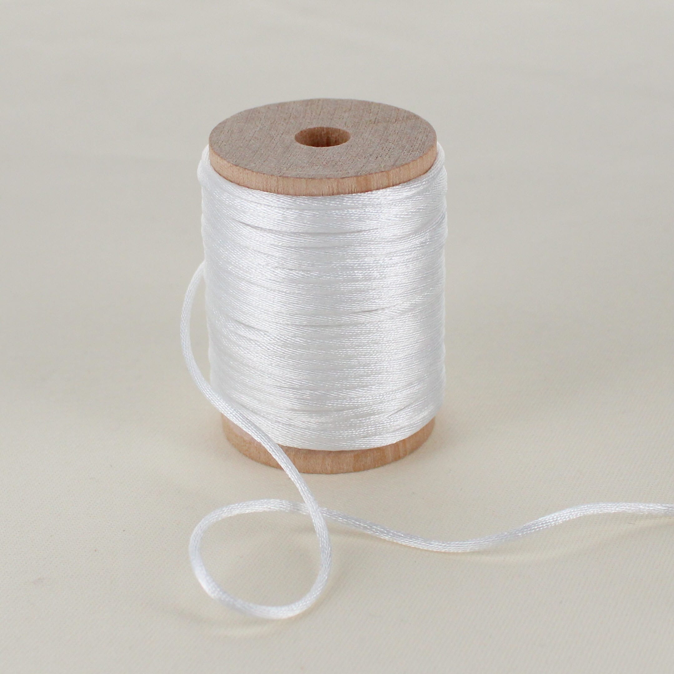 off white satin cord trim on wooden spool sitting on table