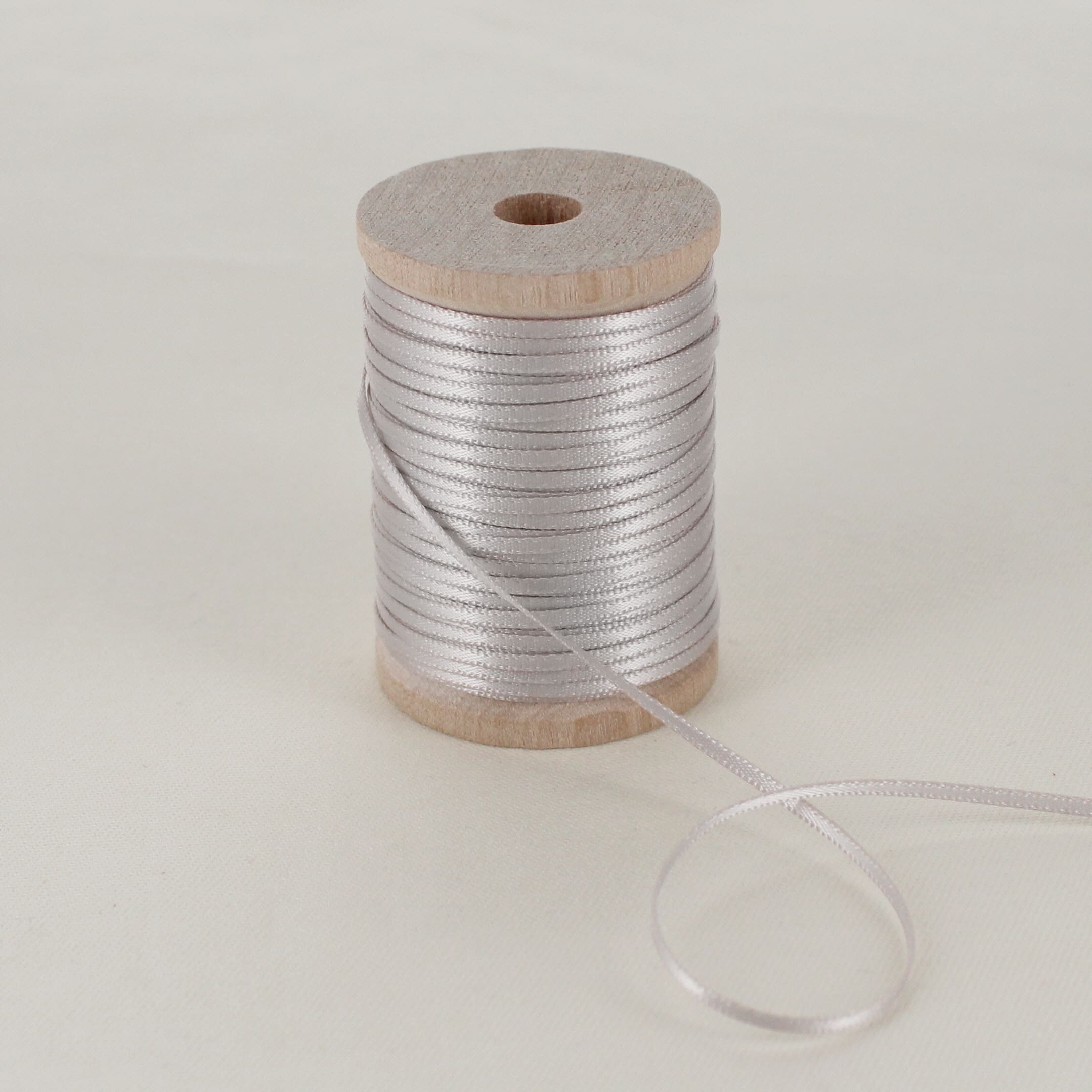silver gray thin satin ribbon on wooden spool sitting on table