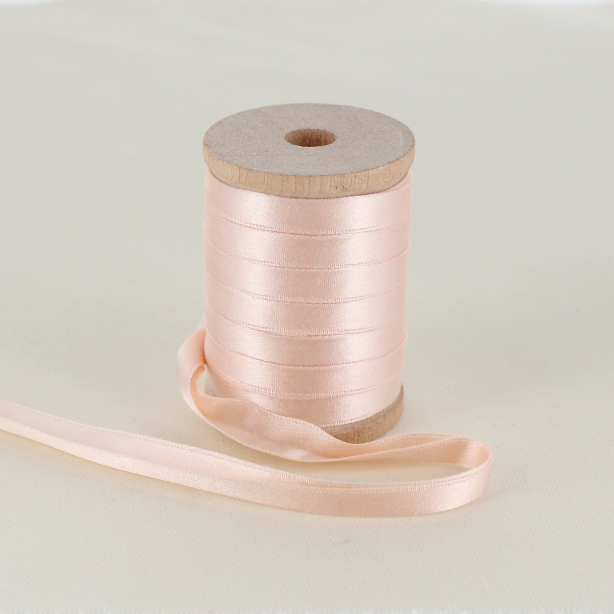 pink folded satin ribbon on wooden spool sitting on table