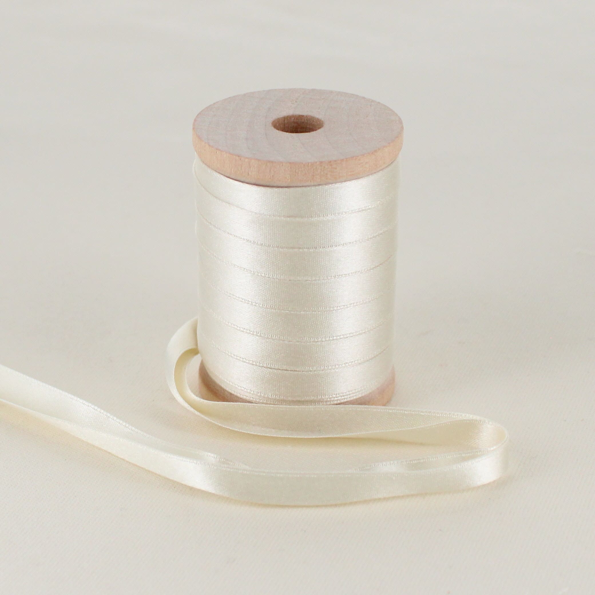 ivory folded satin ribbon on wooden spool sitting on table