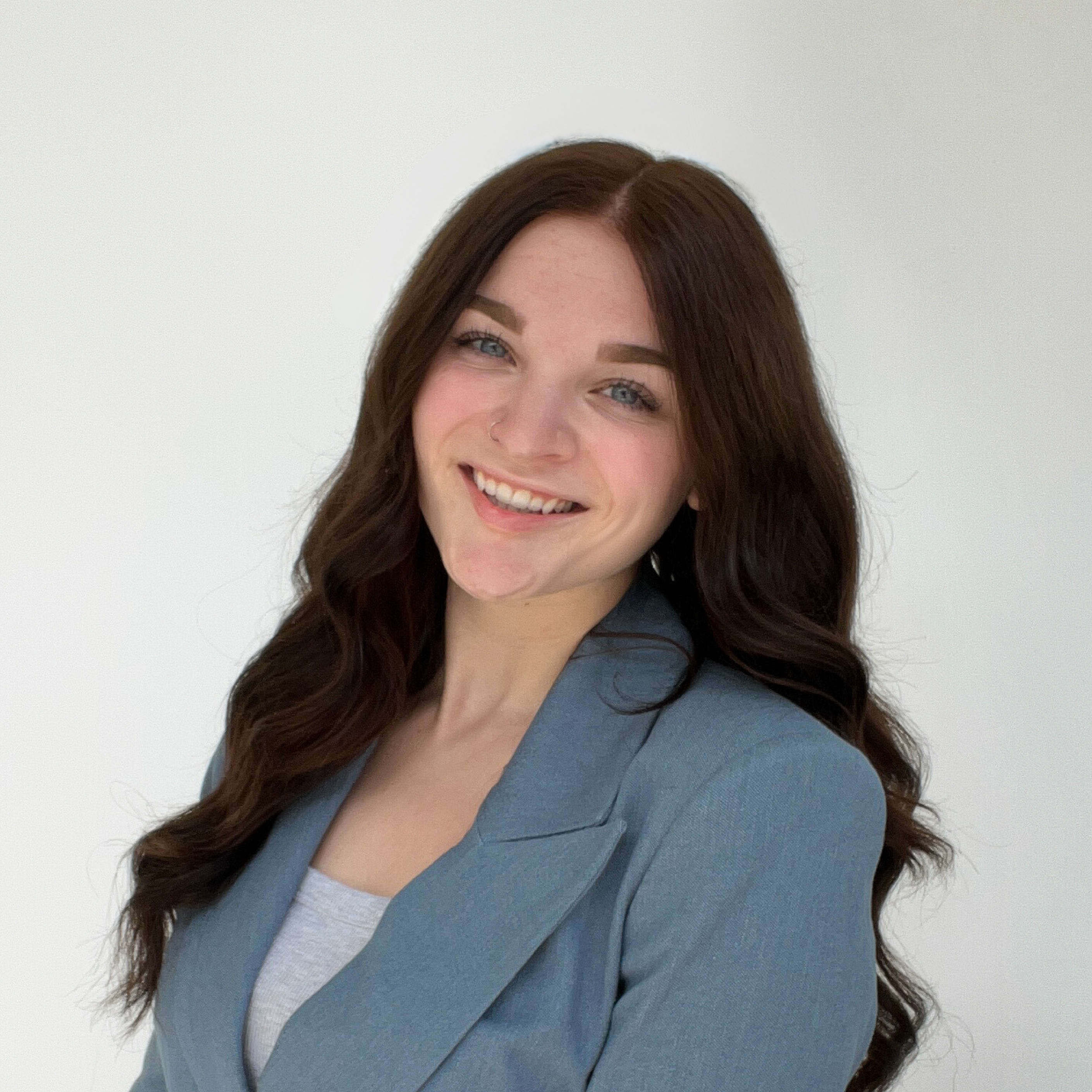 young professional woman in blue blazer standing against white wall smiling at camera