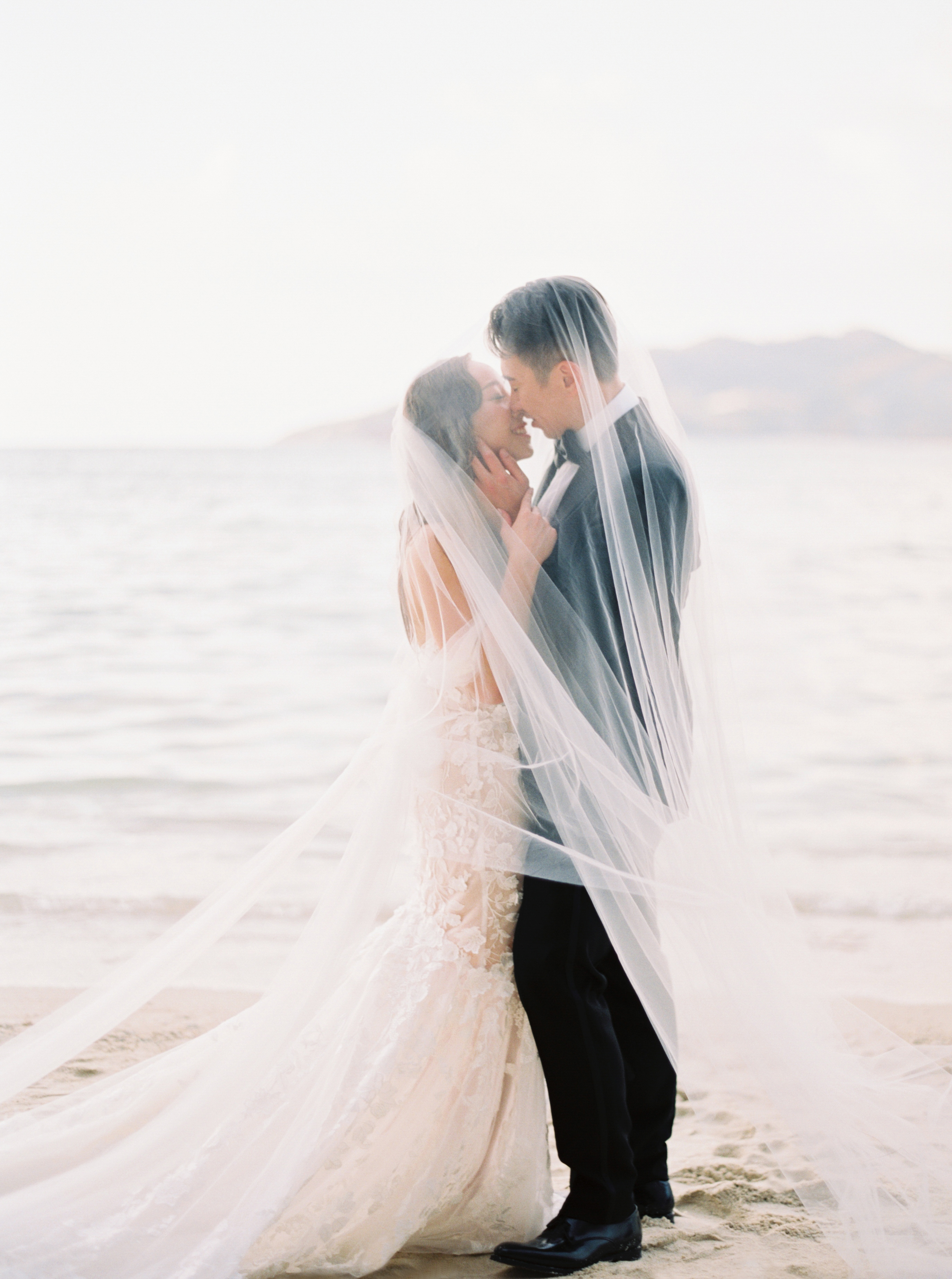 Veil and groom on beach surrounded by soft sara gabriel veil