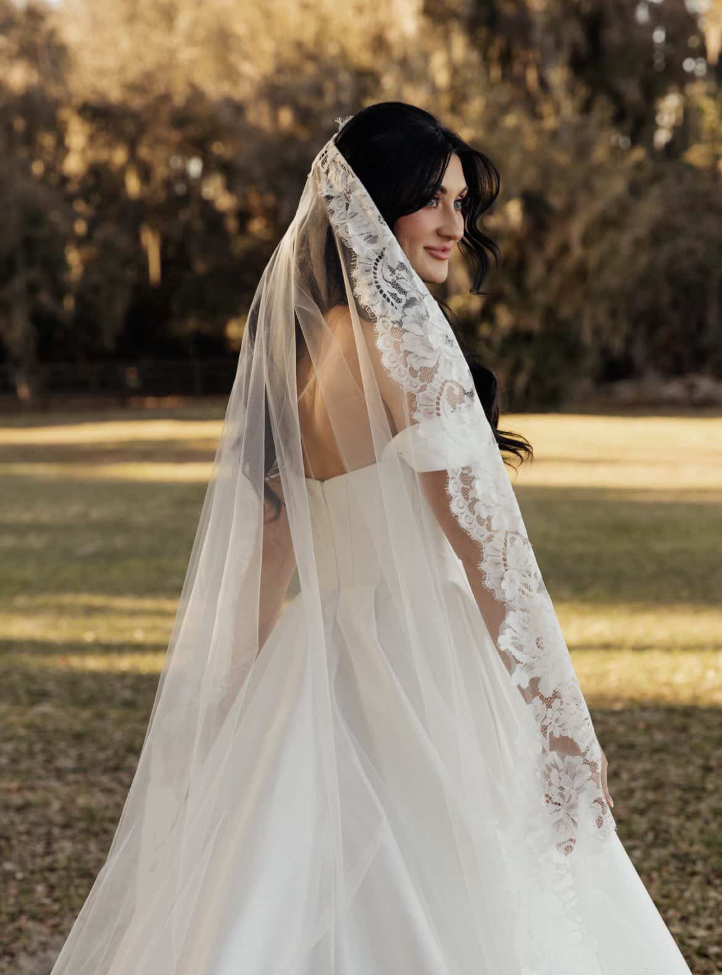 Bride wearing a cathedral-length tulle wedding veil with a wide, intricate floral lace border