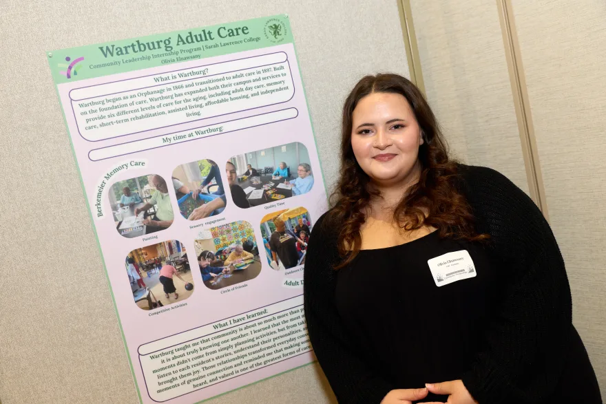 Person smiling beside a presentation board titled "Wartburg Adult Care" with text and photos about care services and personal experiences.