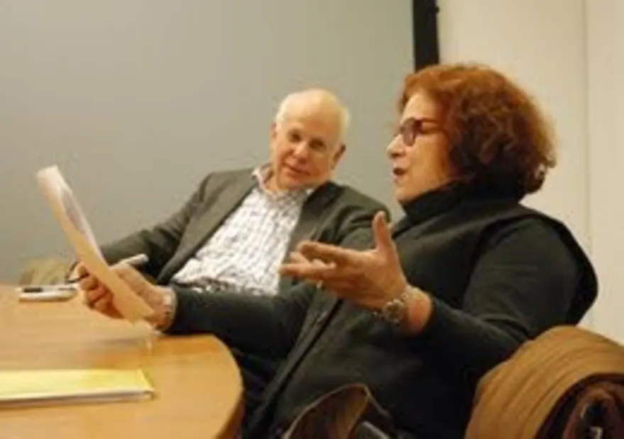 Two people having a discussion at a table, one holding a piece of paper while the other gestures.
