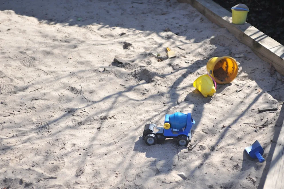 Children's toys scattered on sandy ground with shadows.