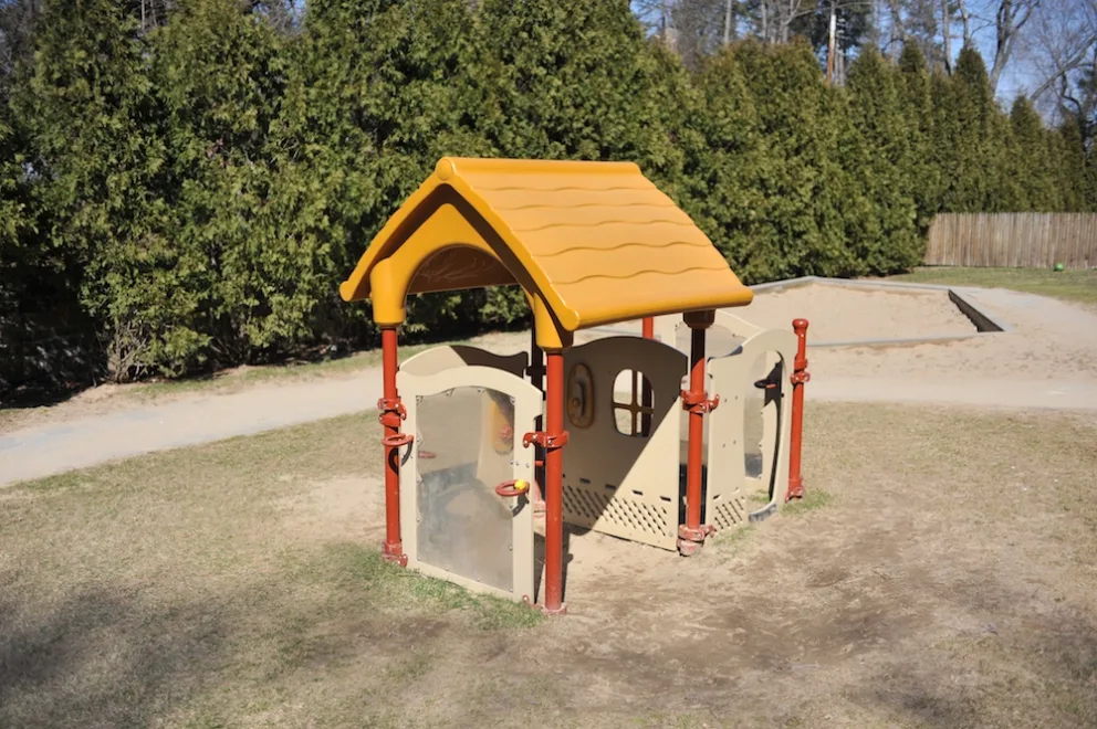 Small playhouse with orange roof in a playground setting.