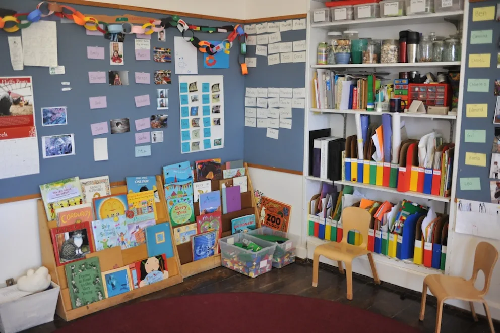 Classroom corner with book display, shelves of supplies, and paper decorations.
