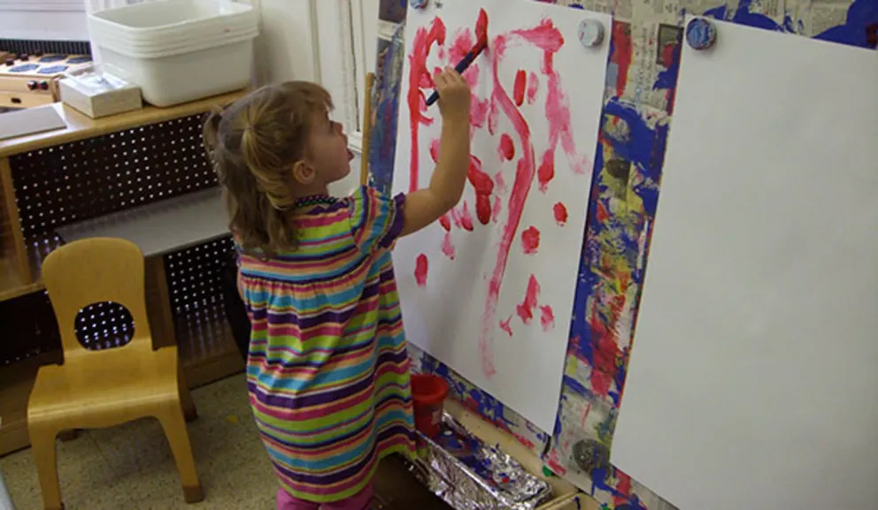 Child painting on a large paper canvas in a colorful smock.