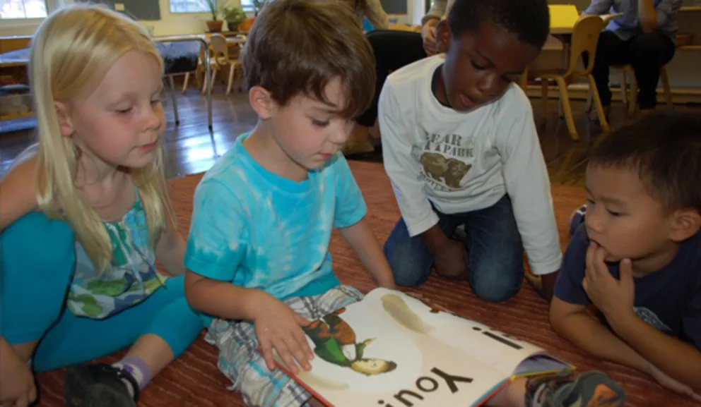 Four children focused on reading a large book together.