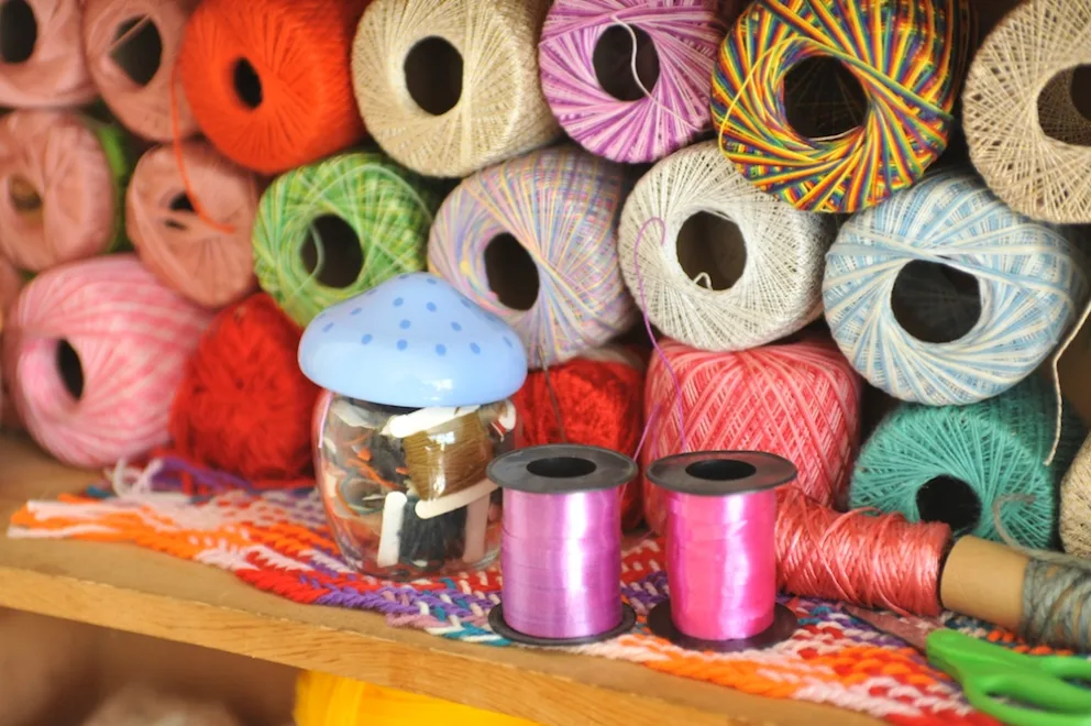 Colorful yarn spools on a shelf with a mushroom-shaped object and thread spools in the foreground.