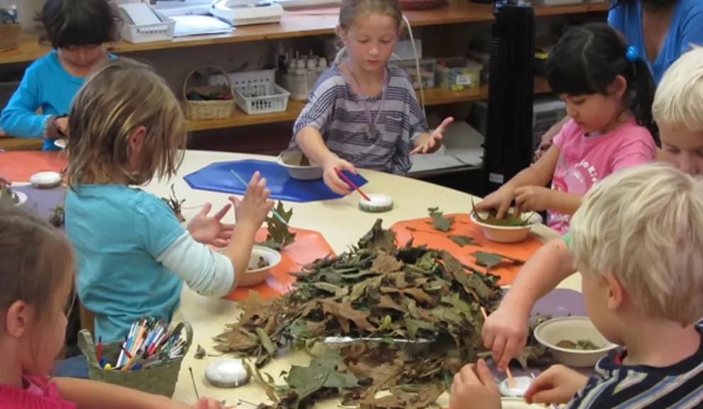 Children engaged in a craft activity with leaves on a table.