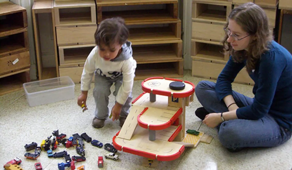 A child and an adult sitting on the floor playing with a toy car garage and various cars.