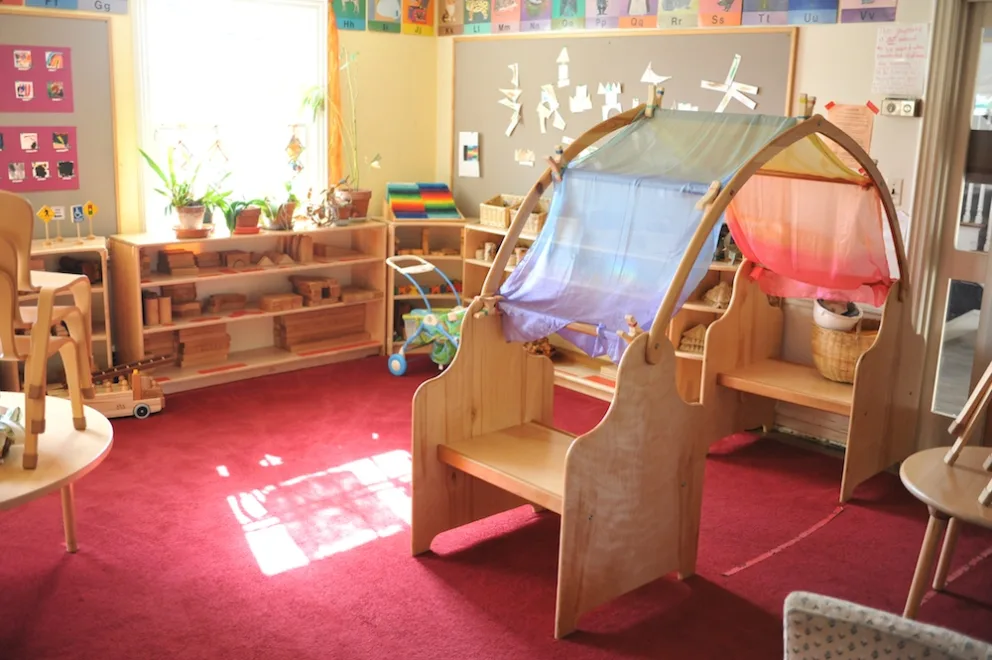 Brightly lit classroom with play area, toys, and educational materials.