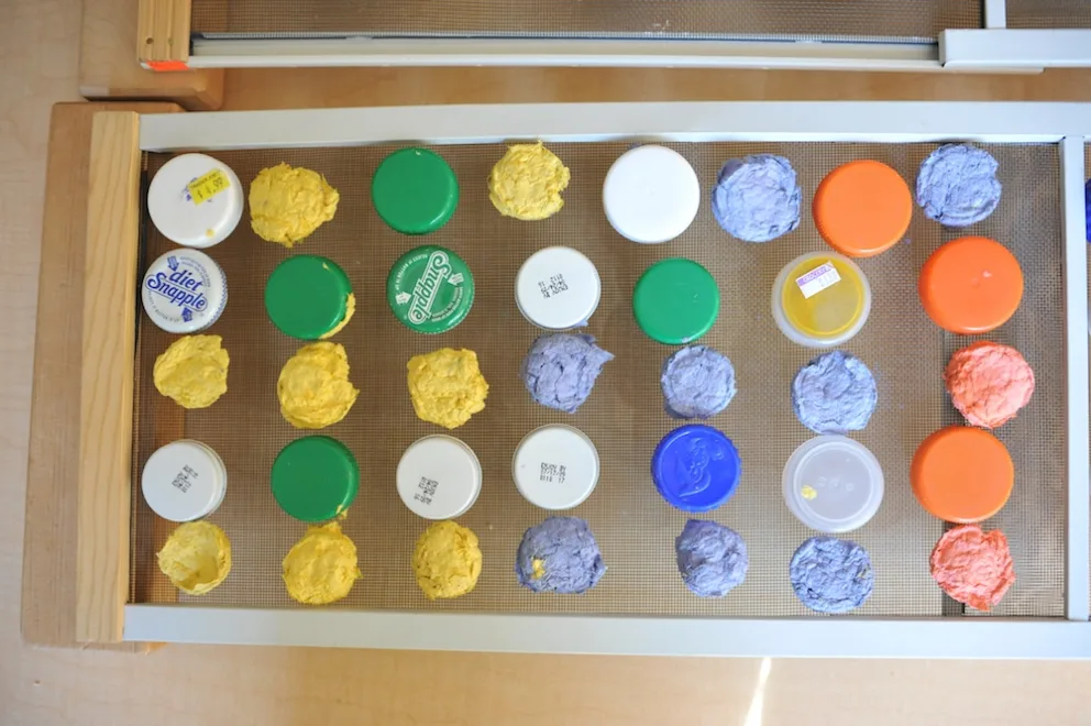 Assorted painted bottle caps arranged in rows on a textured surface.