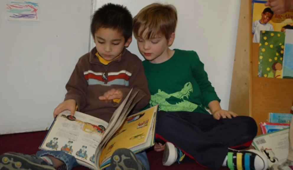 Two children sitting on the floor reading a book together.