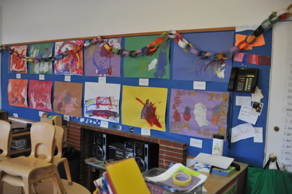 Children's artwork displayed on a colorful classroom wall with a paper chain-decoration.