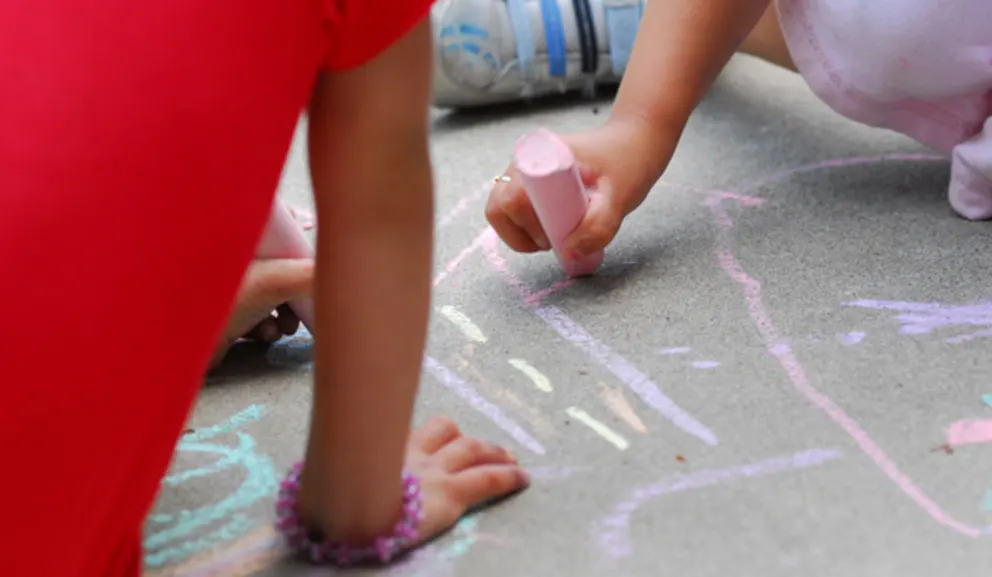 Child drawing with chalk on pavement.