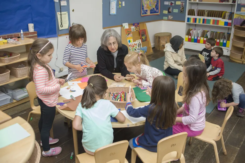 Adult supervising children engaged in arts and crafts in a classroom.