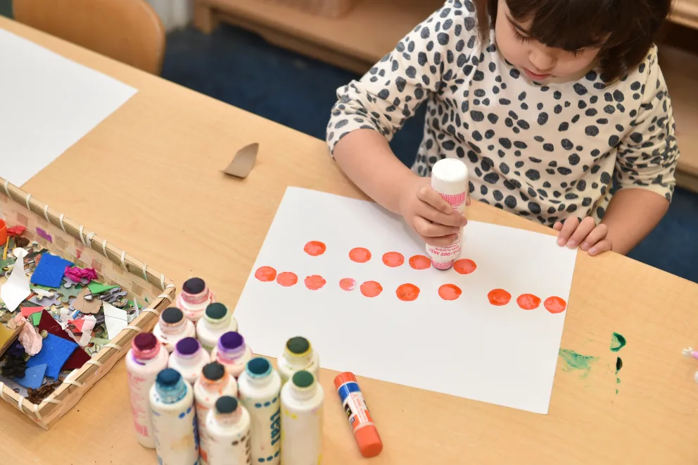 Child doing artwork with paint and paper at a table.