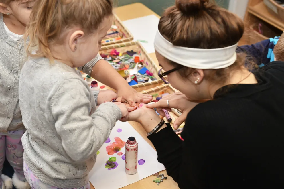 Adult assisting a child with crafts, paint supplies on table.