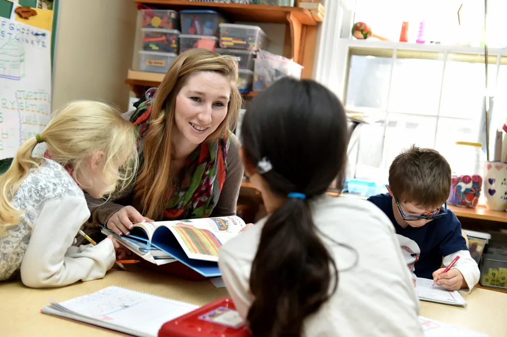 Teacher with three students reading a book in a classroom.