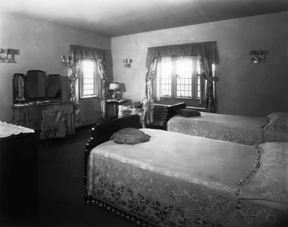 Vintage room with two beds, a dresser, and draped windows.