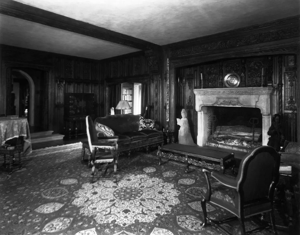 Vintage room with ornate wood paneling, furniture, fireplace, and patterned rug.