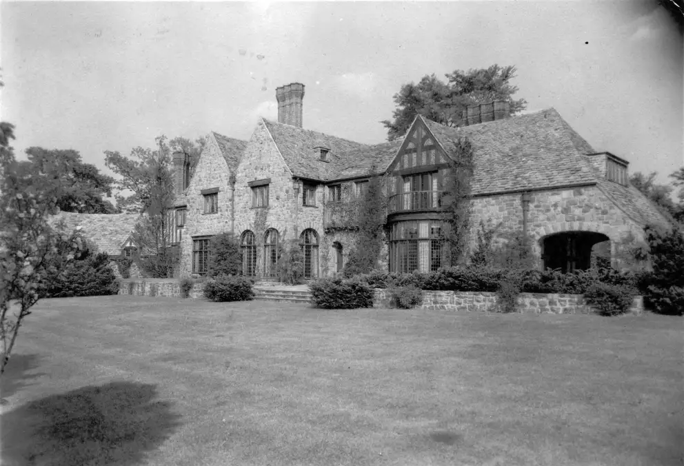 Vintage black and white photo of a large stone house with a garden.