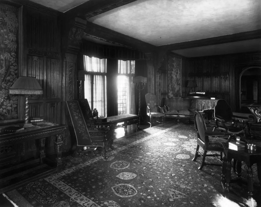 Historic room with ornate wooden panels, furniture, piano, and patterned carpet.