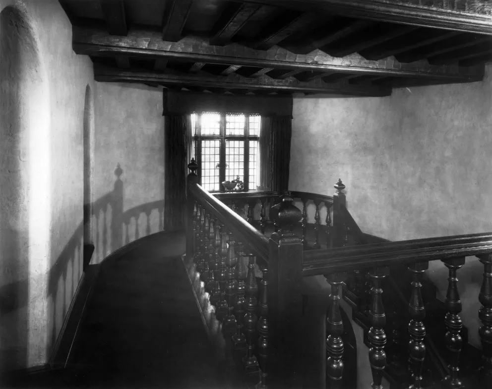 Vintage photo of an interior with a wooden staircase and balustrade, casting a shadow on the wall.
