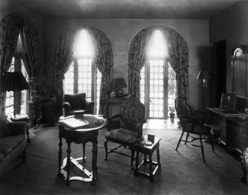 Elegant room with arched windows, curtains, antique furniture, and a writing desk.