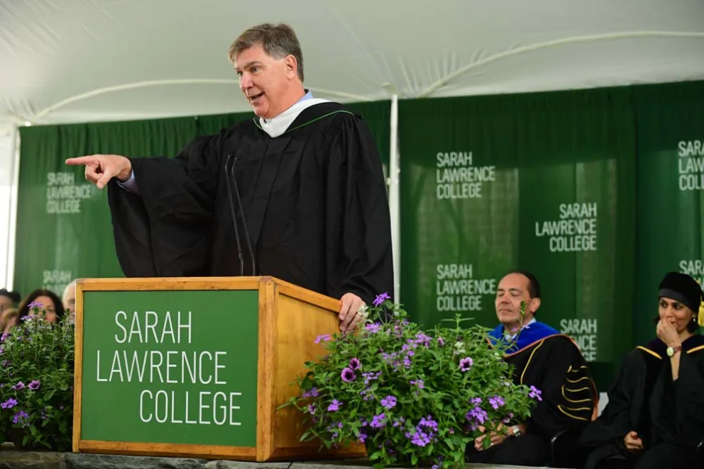 Person speaking at a podium with "Sarah Lawrence College" banner at a formal event.