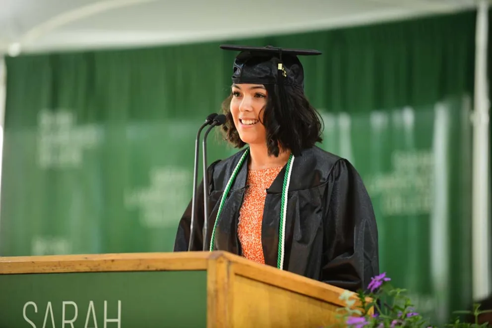 Person in graduation attire speaking at podium.