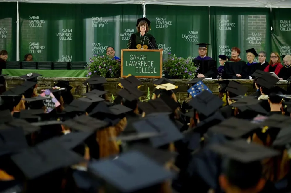 Speaker at podium with graduates in caps at Sarah Lawrence College ceremony.