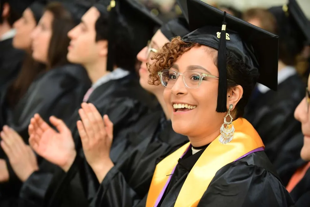 Graduates in caps and gowns clapping at a ceremony.