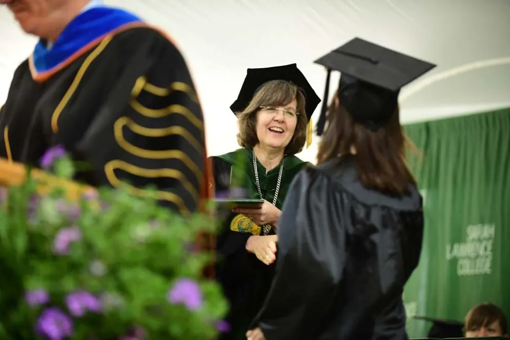 Individual in academic regalia smiling at a graduate during a ceremony.