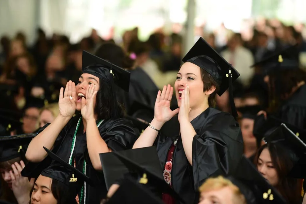 Graduates in caps and gowns cheering at a ceremony.