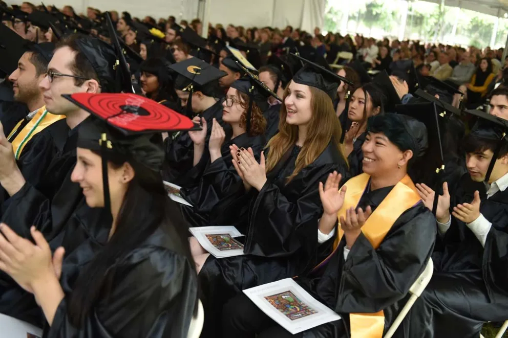 Group of graduates in caps and gowns clapping at a ceremony.
