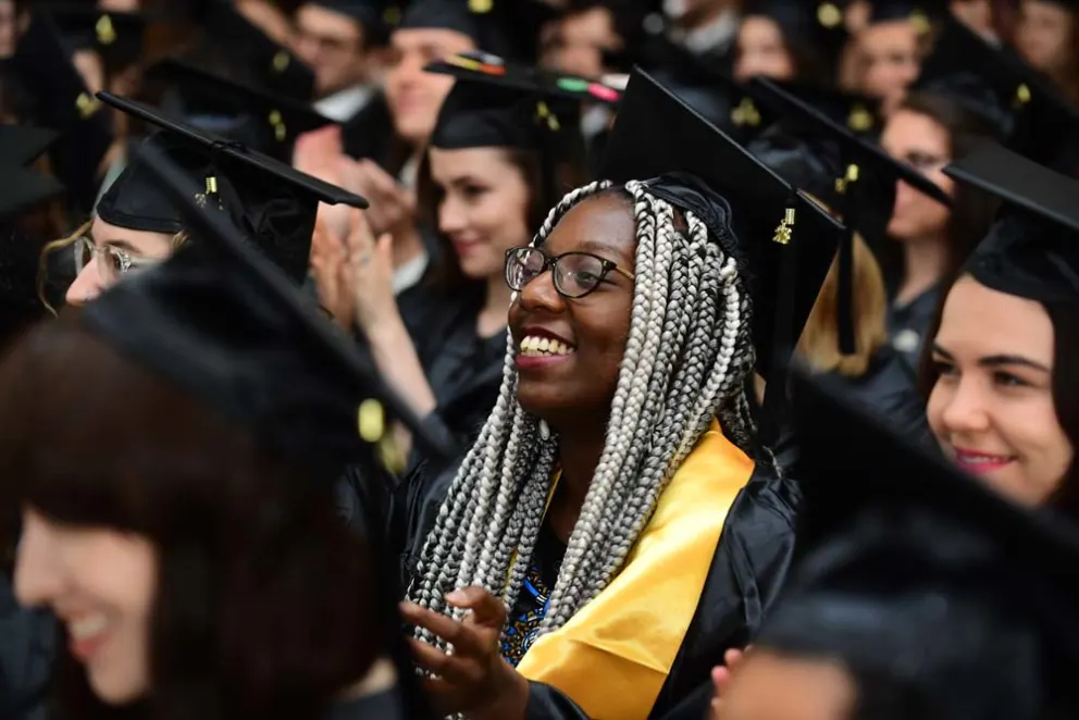 Graduating student in cap and gown smiling amid crowd.